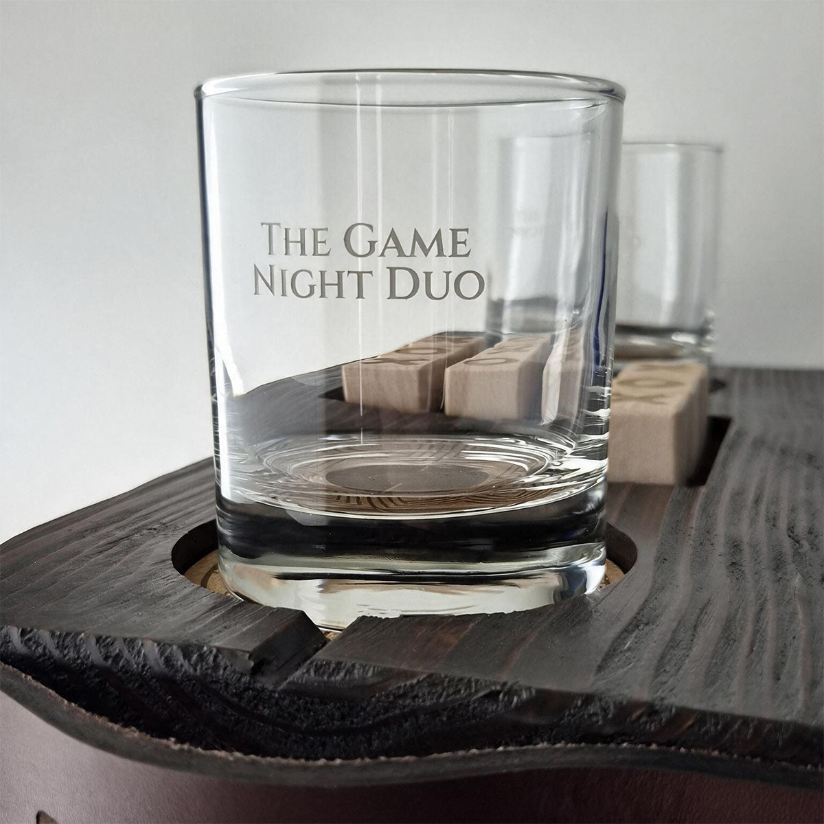 Close-up van twee gegraveerde whiskyglazen en houten speelblokjes op The Game Night Duo.