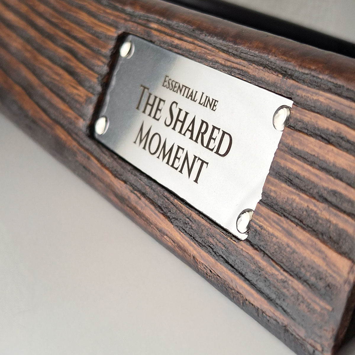 Close-up van de metalen The Shared Moment merkplaat op de massief houten serveerplank.