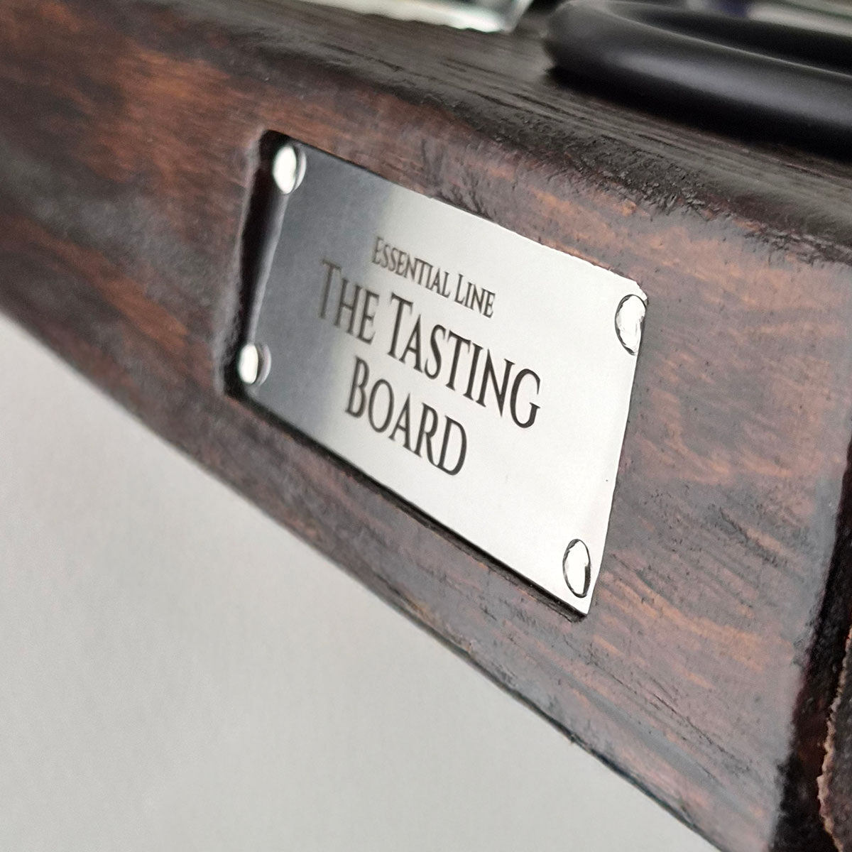 Close-up van de metalen The Tasting Board merkplaat op de massief houten serveerplank.