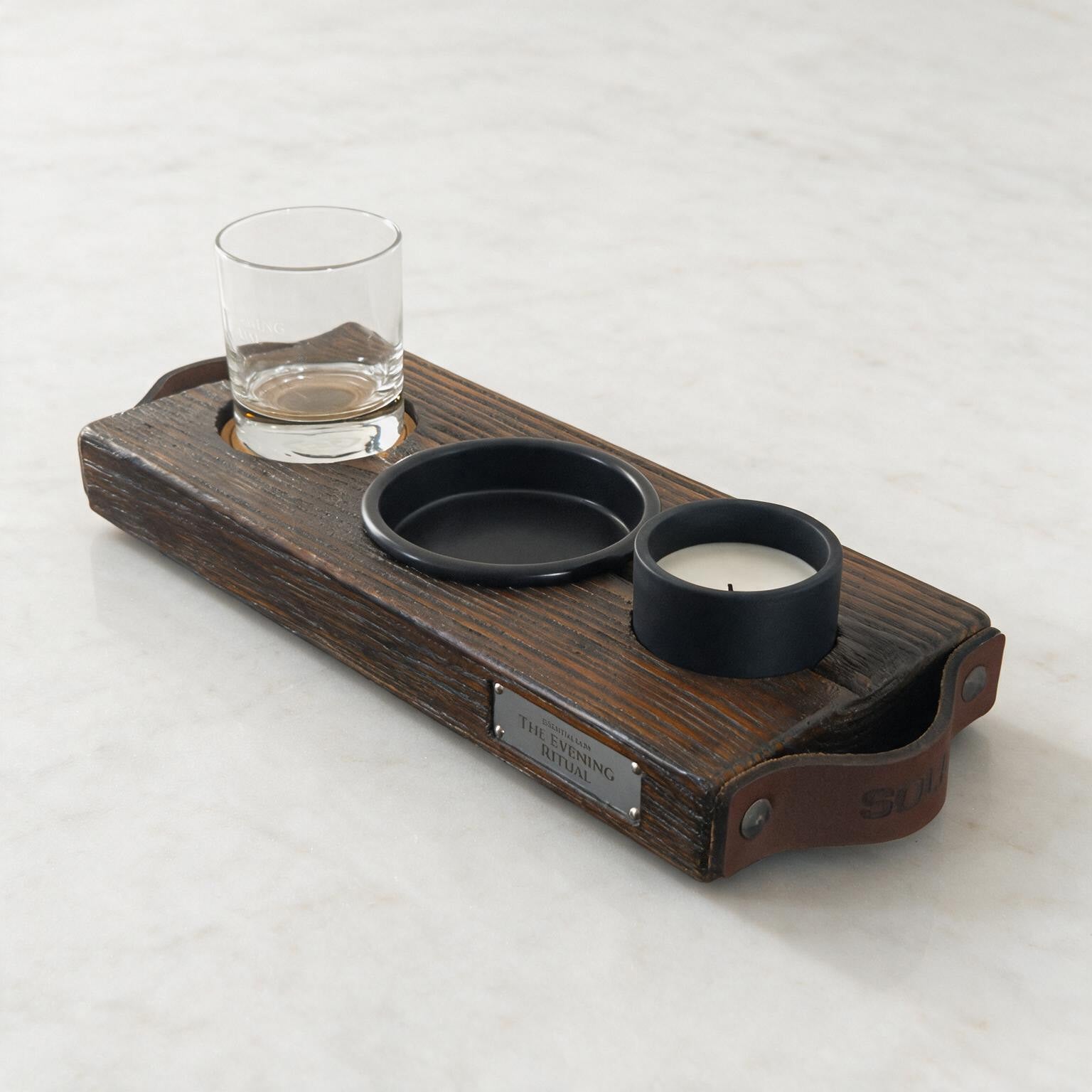 Schuin bovenaanzicht van The Evening Ritual met gegraveerd glas, zwart schaaltje, kaars en metalen naamplaatje