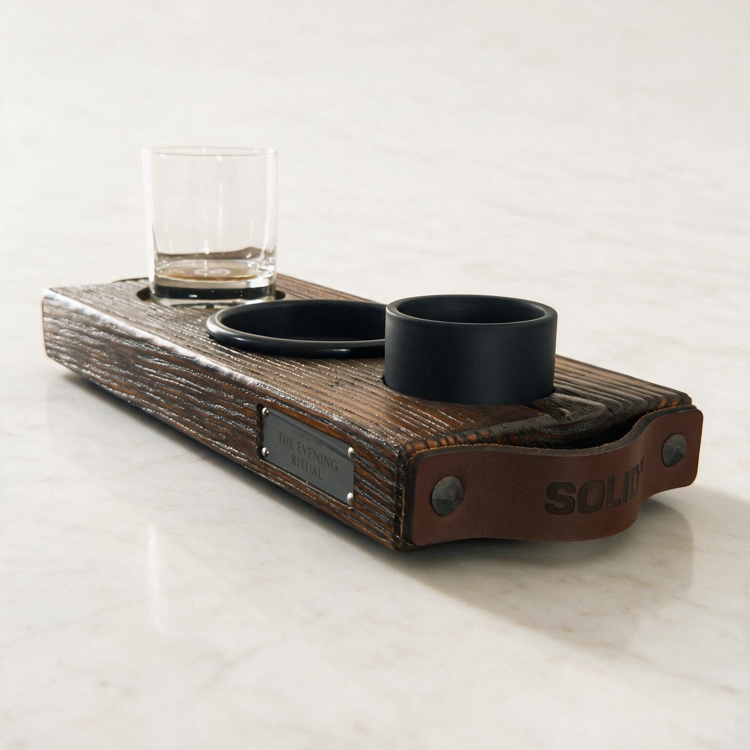The Evening Ritual van donker massief hout met leren handgrepen, gegraveerd glas, zwart schaaltje en kaars op wit steen